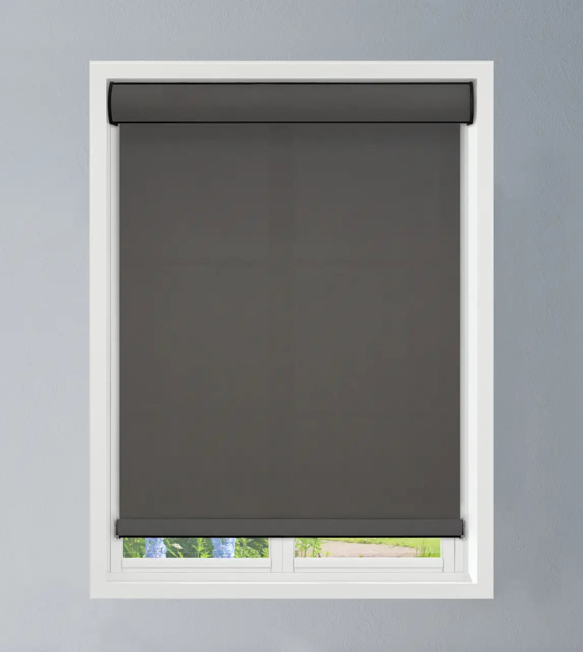 Dark gray roller shade mounted above a white-framed window overlooking a green outdoor view, shade in raised position